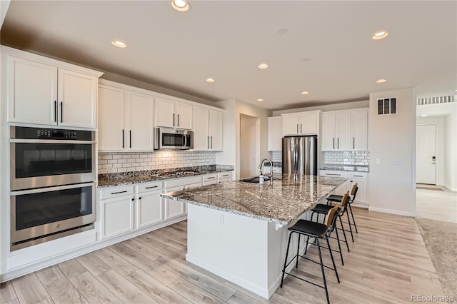 kitchen featuring appliances with stainless steel finishes, white cabinetry, an island with sink, sink, and dark stone counters