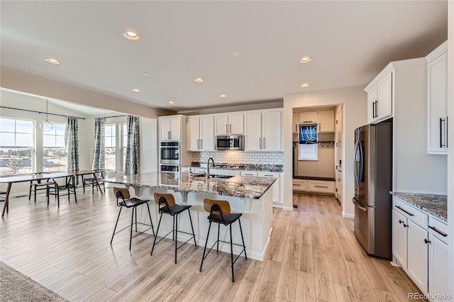 kitchen with white cabinets, an island with sink, dark stone counters, and appliances with stainless steel finishes