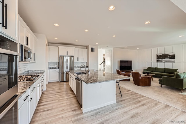 kitchen with white cabinetry, sink, a kitchen bar, a kitchen island with sink, and stainless steel appliances