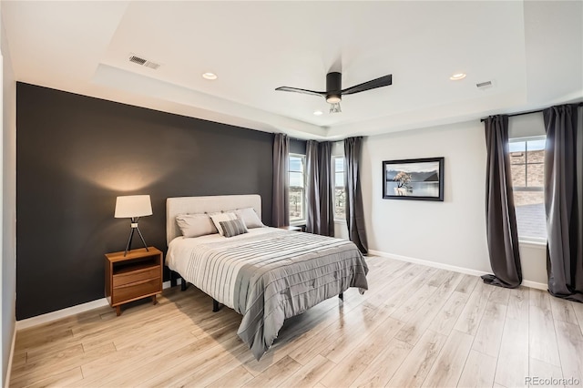 bedroom featuring ceiling fan, a raised ceiling, and light wood-type flooring