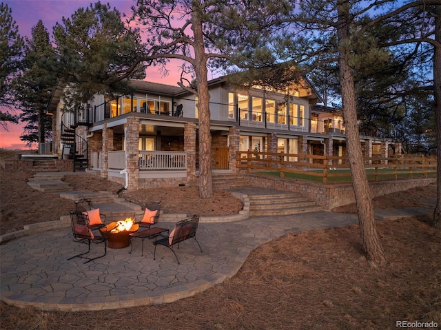 back house at dusk with a fire pit, a patio, and a balcony