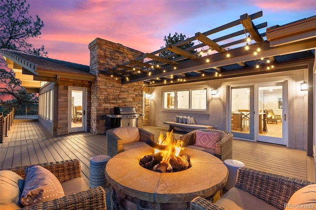 deck at dusk featuring a pergola, grilling area, and an outdoor fire pit