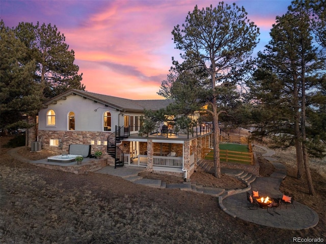 back house at dusk featuring a balcony, a patio, a fire pit, and central air condition unit