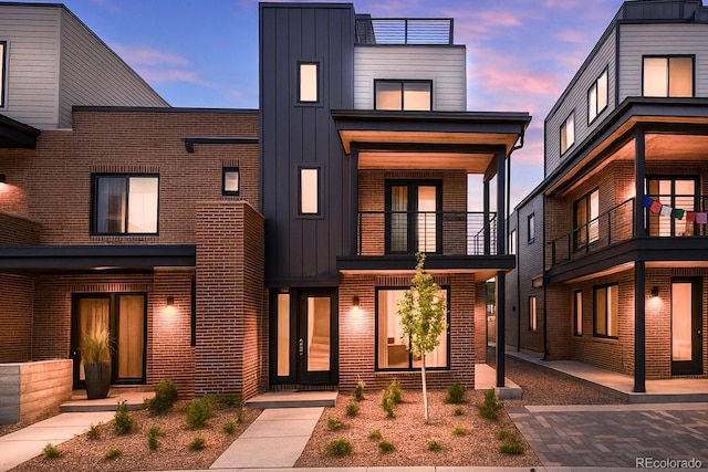 view of front of house featuring board and batten siding, a balcony, and brick siding