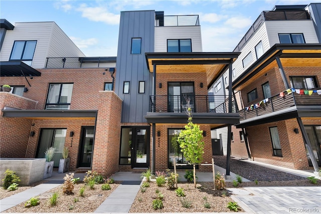 view of front of property featuring board and batten siding, a balcony, and brick siding
