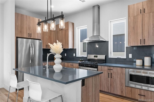 kitchen featuring appliances with stainless steel finishes, wall chimney exhaust hood, dark countertops, a sink, and light wood-type flooring