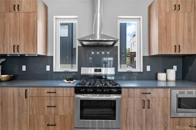 kitchen with appliances with stainless steel finishes, wall chimney range hood, modern cabinets, decorative backsplash, and brown cabinetry