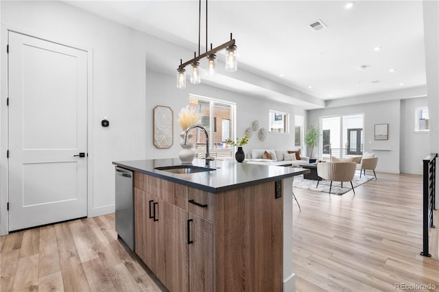 kitchen with a sink, dark countertops, light wood-type flooring, a kitchen island with sink, and modern cabinets