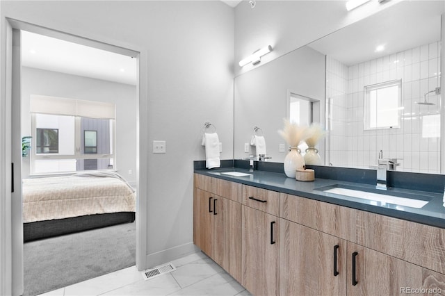 ensuite bathroom with double vanity, baseboards, a tile shower, and marble look tile flooring