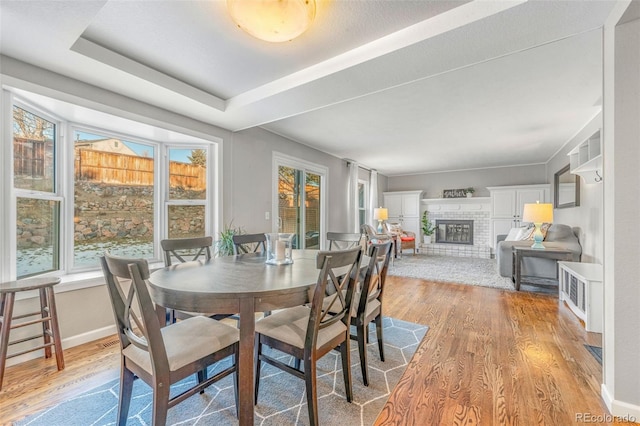 dining room featuring light hardwood / wood-style floors, a tray ceiling, and a brick fireplace