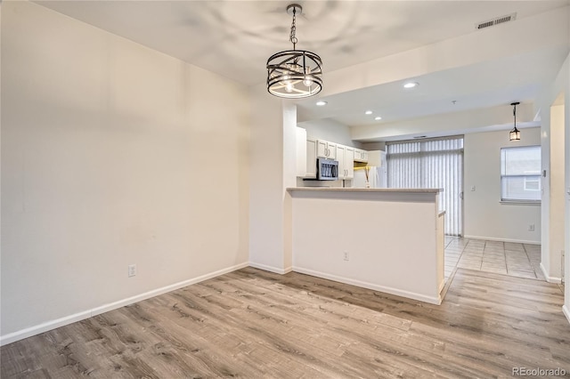 kitchen with pendant lighting, white cabinets, a chandelier, kitchen peninsula, and light hardwood / wood-style flooring