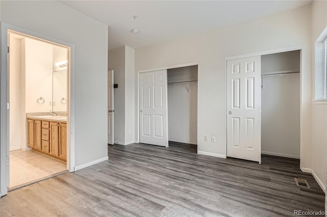 unfurnished bedroom with two closets, ensuite bathroom, and hardwood / wood-style flooring