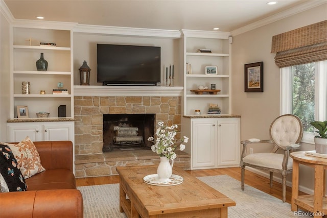 living room with ornamental molding, a stone fireplace, built in features, and light wood-type flooring