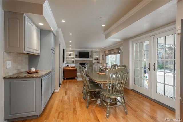 dining space with ornamental molding, french doors, a fireplace, and light wood finished floors