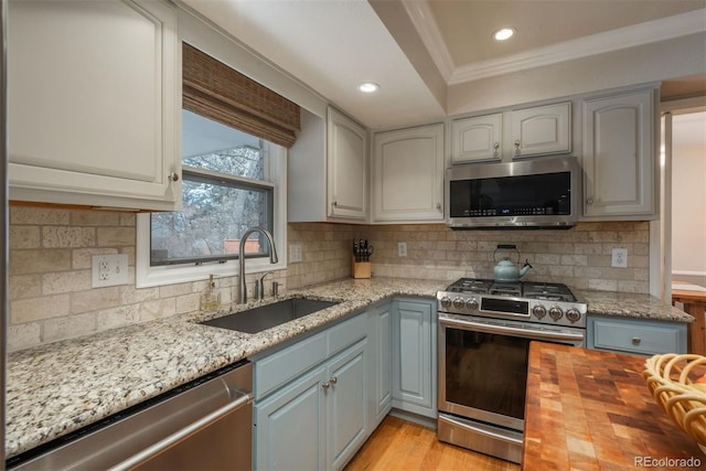 kitchen featuring sink, ornamental molding, stainless steel appliances, light stone countertops, and decorative backsplash