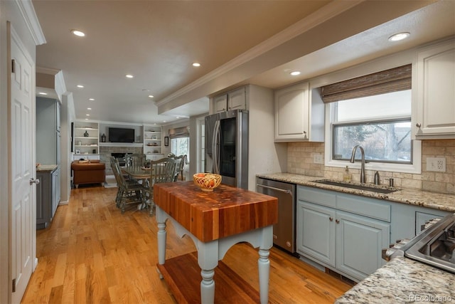 kitchen with a fireplace, crown molding, stainless steel appliances, open floor plan, and a sink