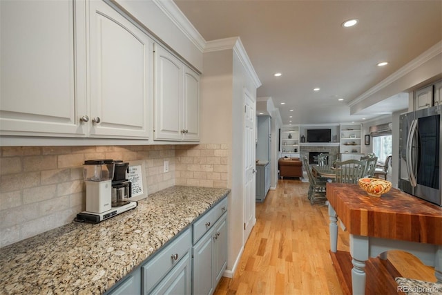 kitchen with light wood-type flooring, a fireplace, white cabinetry, and crown molding