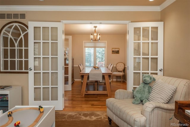 sitting room with a notable chandelier, visible vents, ornamental molding, wood finished floors, and baseboards