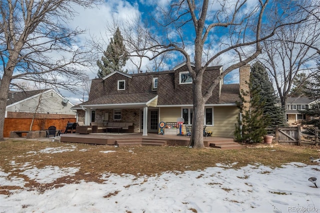 snow covered back of property with an outdoor living space and a deck