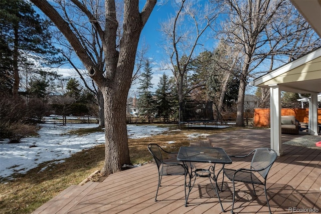 snow covered deck with a trampoline and fence