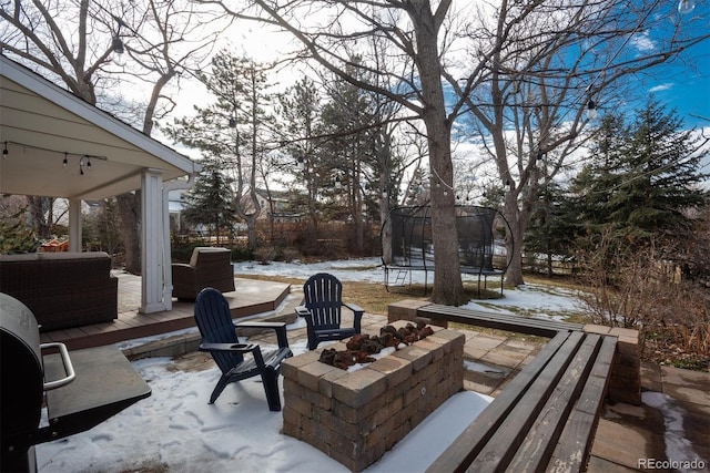 snow covered patio with a trampoline, an outdoor fire pit, and a wooden deck