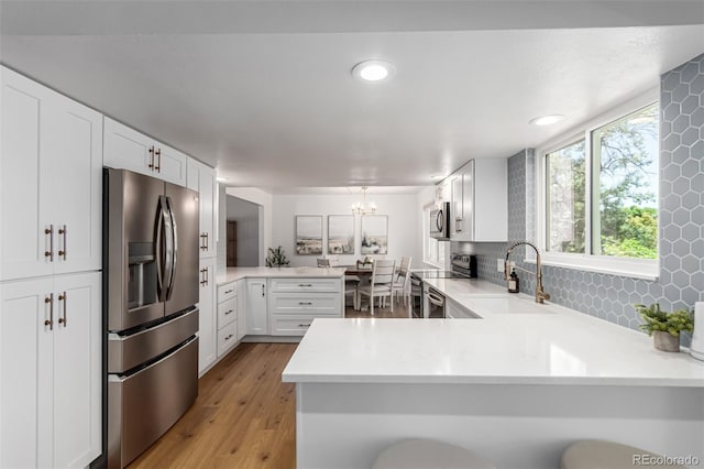 5914 S Kearney St, Centennial, CO 80111 - kitchen featuring stainless steel appliances, a peninsula, light countertops, tasteful backsplash, and light wood-type flooring