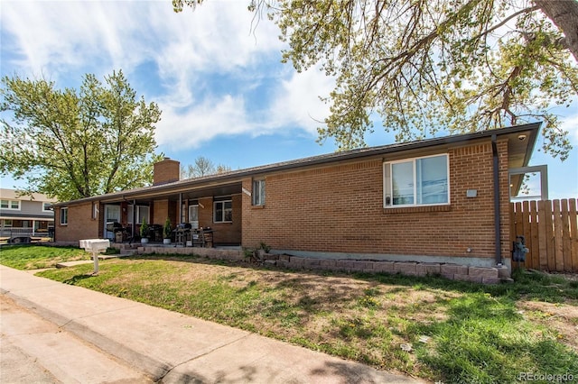 ranch-style house featuring fence, a front yard, a chimney, brick siding, and a patio area