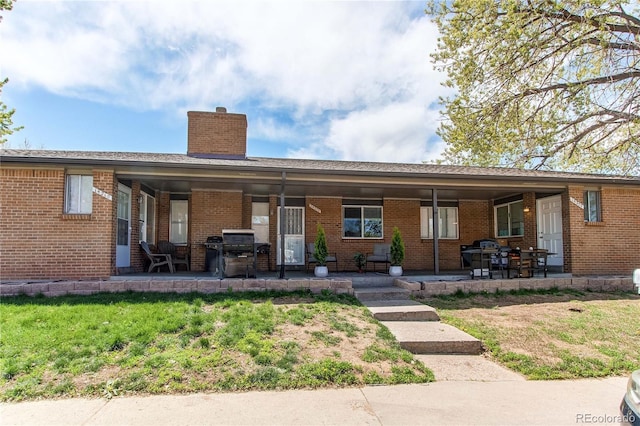 rear view of property featuring a lawn, a patio, a chimney, and brick siding