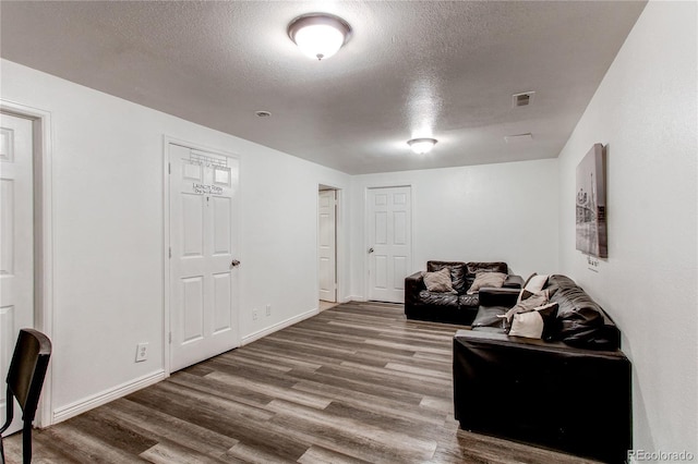living room featuring baseboards, a textured ceiling, visible vents, and wood finished floors