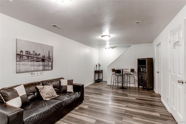 living room featuring wood finished floors, baseboards, a textured ceiling, and visible vents