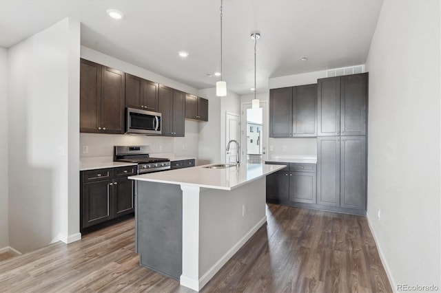 kitchen featuring a sink, stainless steel appliances, wood finished floors, light countertops, and baseboards