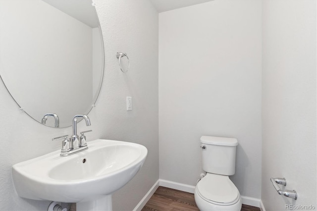 half bathroom with a sink, toilet, baseboards, and wood finished floors
