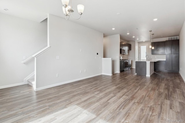 unfurnished living room featuring a sink, an inviting chandelier, light wood-style flooring, and baseboards