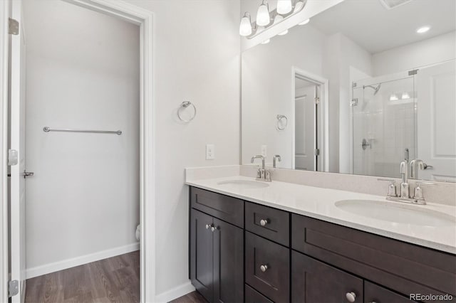 bathroom featuring double vanity, wood finished floors, a shower stall, and a sink