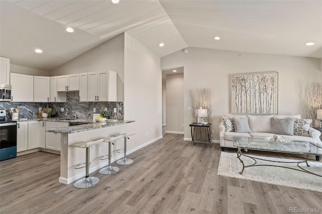 kitchen with white cabinetry, kitchen peninsula, vaulted ceiling, appliances with stainless steel finishes, and light wood-type flooring