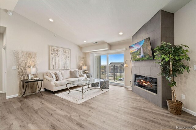 living room with light wood-type flooring, vaulted ceiling, and a tiled fireplace