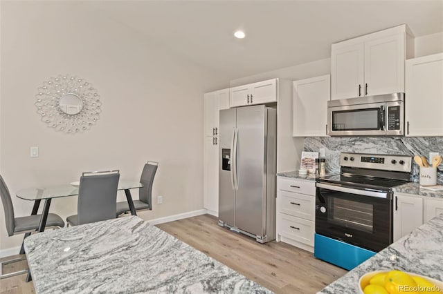 kitchen with light stone counters, white cabinets, light wood-type flooring, and appliances with stainless steel finishes