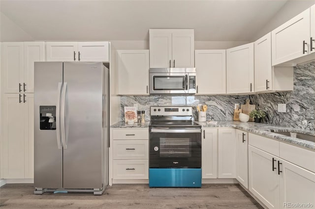 kitchen with white cabinets, stainless steel appliances, light stone counters, and light hardwood / wood-style flooring