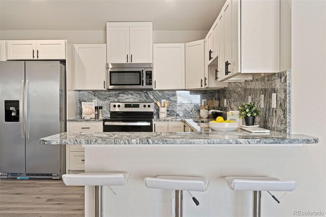 kitchen with white cabinets, light hardwood / wood-style flooring, light stone counters, appliances with stainless steel finishes, and a kitchen bar