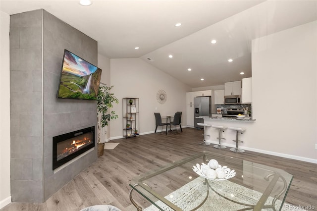 living room with light wood-type flooring, lofted ceiling, and a tile fireplace