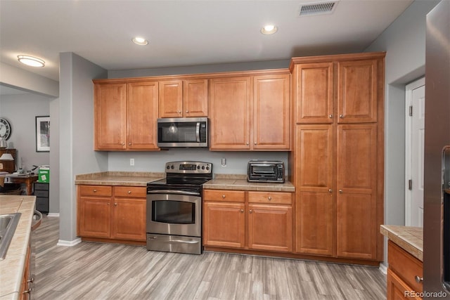 kitchen with tile countertops, light wood-type flooring, and appliances with stainless steel finishes