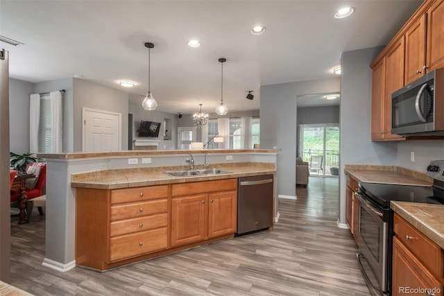 kitchen featuring sink, decorative light fixtures, light wood-type flooring, appliances with stainless steel finishes, and a notable chandelier