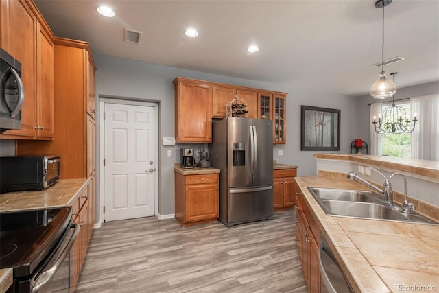 kitchen featuring stainless steel appliances, sink, tile countertops, decorative light fixtures, and a notable chandelier