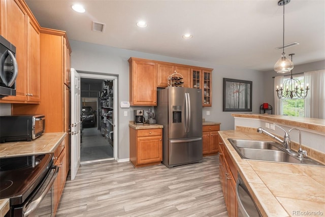 kitchen featuring tile counters, sink, stainless steel appliances, a notable chandelier, and light wood-type flooring