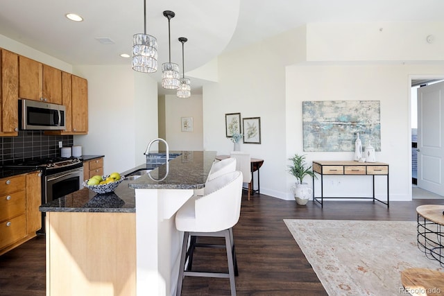 1650 Fillmore St Unit 504, Denver, CO 80206 - kitchen featuring brown cabinetry, dark wood-style flooring, a sink, dark stone countertops, and appliances with stainless steel finishes
