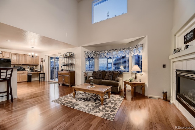 living room featuring a tile fireplace, light hardwood / wood-style flooring, a towering ceiling, and an inviting chandelier