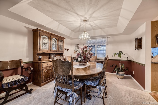 dining area featuring wood walls, light colored carpet, and a tray ceiling