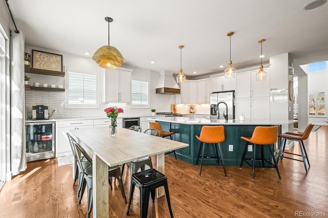kitchen with beverage cooler, white cabinetry, backsplash, light countertops, and premium range hood