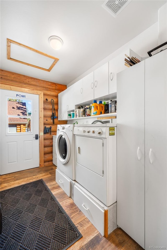 clothes washing area with dark wood-type flooring, rustic walls, washer and clothes dryer, and cabinets