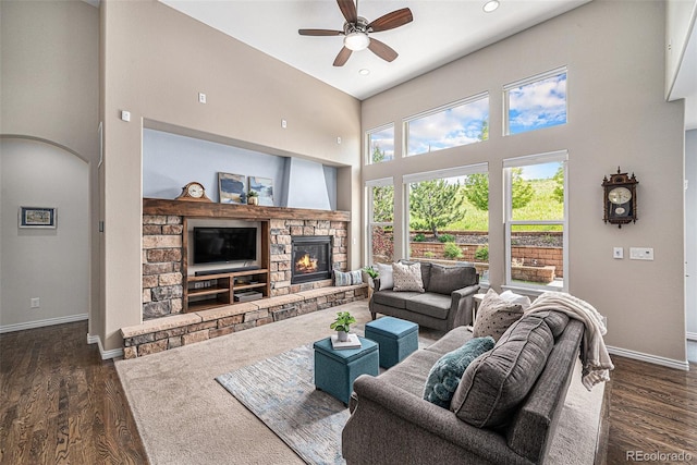 13942 W 87th Dr, Arvada, CO 80005 - living room featuring a ceiling fan, baseboards, a towering ceiling, a stone fireplace, and dark wood-type flooring